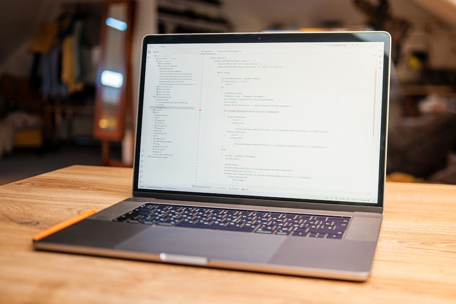 A photograph displays a close-up of a computer screen showing lines of HTML code with syntax highlighting; the code includes tags such as <table> and <td>, with attributes like width, height, colspans